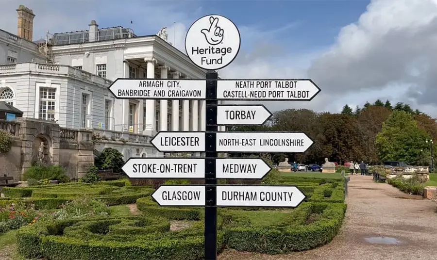 Sign post with "Heritage Fund" at the top, showing signs to 9 places: Stoke on Trent (Midlands & East) Leicester (Midlands & East) County Durham (North) North-East Lincolnshire (North) Torbay (London & South) Medway (London & South) Glasgow (Scotland) Armagh City, Banbridge and Craigavon (Northern Ireland) Neath Port Talbot (Wales)