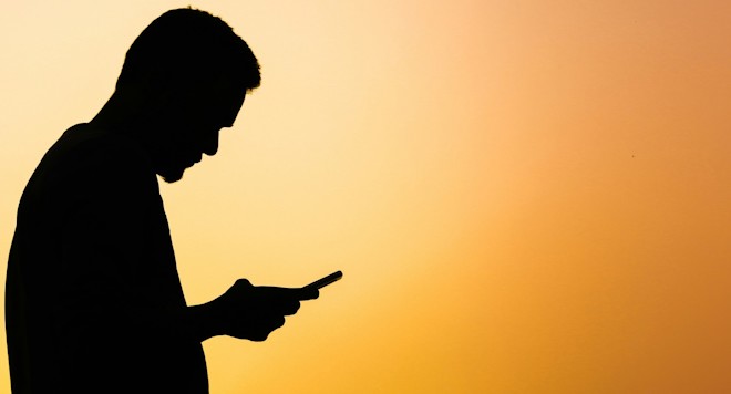 Image of shadow of a man using staring at their phone in front of orange background