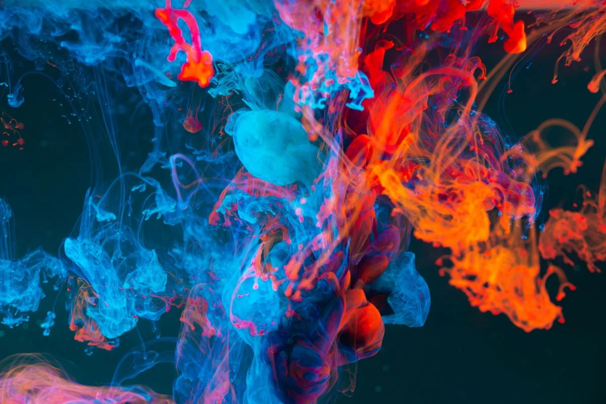 Image illustrates Vibrant swirls of blue, red, and orange ink blend and diffuse in water, creating a colorful abstract pattern against a dark background.