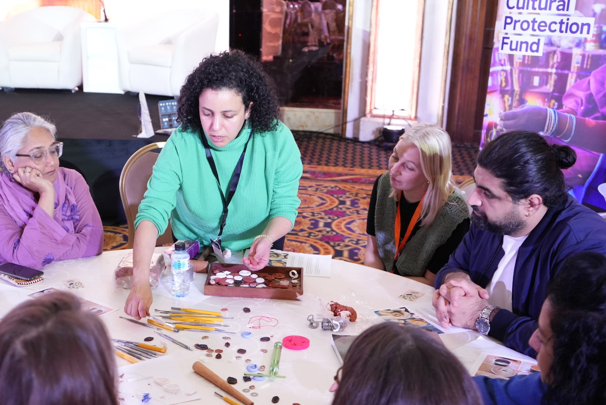 A diverse group of individuals seated around a table with a woman positioned at the center, engaged in discussion.