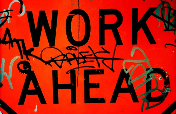 words "WORK AHEAD" displayed on a red background covered in colourful graffiti