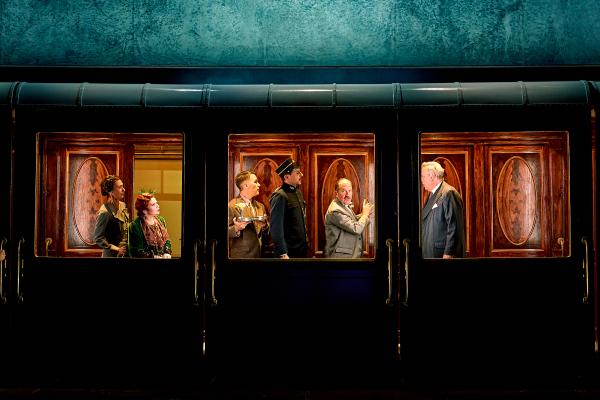 An image of a dark train where you can see people inside the carriages lit up and chatting in period dress