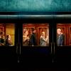 An image of a dark train where you can see people inside the carriages lit up and chatting in period dress