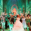 Wizard of Oz performers on stage with their arms stretched upwards in front of a green background